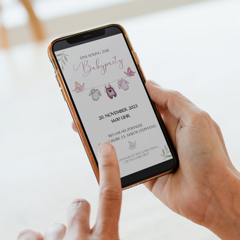 May include: A smartphone displaying a baby shower invitation with a pink and white color scheme. The invitation features a string of clothes hanging with butterflies and the text "EINLADUNG ZUR Babyparty 20. NOVEMBER 2023 14.00 UHR BEI SARAH ZUHAUSE GRIBE 23, 345678 STEPHANS) UM KURZE R&Uuml;CKMELDUNG, OB DU DABEI BIST"