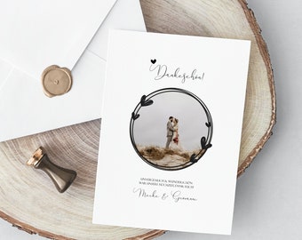 May include: A white card with a black circle frame containing a photo of a couple kissing in a field. The text "Dankeschön!" is at the top of the card. The text "Unvergesslich & wunderschön war unsere Hochzeit. Dank euch!" is below the photo. The text "Meike & Giovanni" is at the bottom of the card.