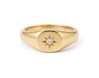 Puede incluir: Un anillo de sello de oro con una banda pulida y lisa y una cara circular plana. El centro de la cara está grabado con un diseño de estrella de ocho puntas, que contiene una pequeña piedra preciosa redonda y transparente en el centro.