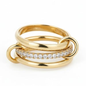 May include: A set of three gold rings. The top and bottom rings are plain gold, and the middle ring is set with small, clear gemstones. The rings are linked together with curved gold connectors.