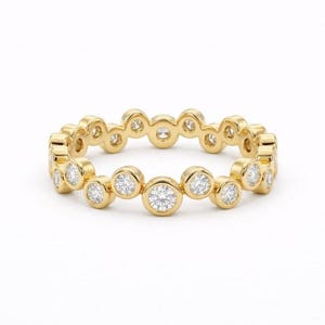 Op de afbeelding: Een gouden ring met een reeks ronde, heldere edelstenen rond de band. De ring is geplaatst tegen een witte achtergrond, waardoor de schittering van de edelstenen en de warme tint van het goud worden benadrukt.