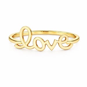 May include: A gold-colored ring spelling out the word "love" in a cursive font. The ring is set against a white background, highlighting the elegant design. The ring is a piece of jewelry.