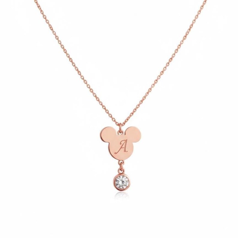 Peut inclure: Collier en or rose avec un pendentif en forme de Mickey Mouse grav&eacute; de la lettre "A". Une petite pierre pr&eacute;cieuse transparente est suspendue en dessous. La cha&icirc;ne est d&eacute;licate et le design est &eacute;l&eacute;gant. Un bijou charmant.