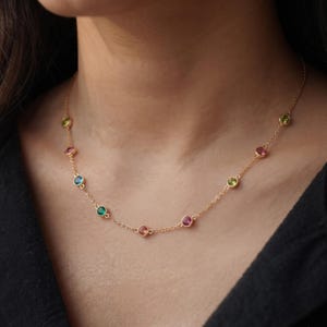 Peut inclure: Un collier à chaîne dorée orné de pierres précieuses rondes serties clos, espacées régulièrement et déclinées en plusieurs couleurs dont le bleu, le vert, le rose et le jaune. La fine chaîne métallique relie chaque sertissage individuel.