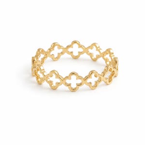 May include: A gold ring featuring a continuous band of repeating openwork quatrefoil shapes. The metal has a polished, reflective finish, and the design consists of interconnected four-petaled floral motifs that form a delicate, uniform circular band.