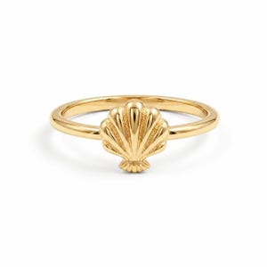 Peut inclure: Une bague en or poli ornée d'un motif central en forme de coquille Saint-Jacques. L'anneau est lisse et circulaire, tandis que l'ornement en coquille présente des stries verticales et une forme en éventail, formant un bijou métallique brillant.