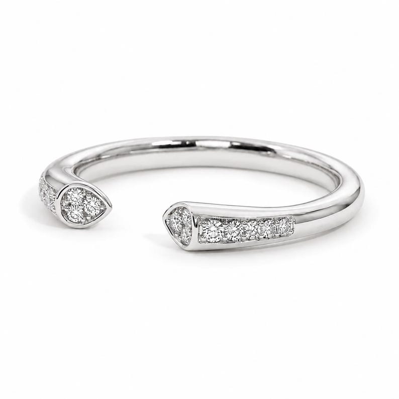 May include: A silver-toned open ring featuring a polished band with two tapered ends. Each end is set with small, clear, round-cut stones, with three stones clustered at the tips and a row of five stones extending along the band's shank.
