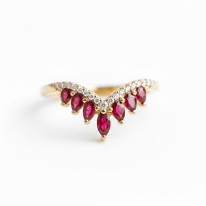May include: A gold ring featuring a V-shaped design. The ring is adorned with marquise-cut red gemstones and small, round white gemstones. The gemstones are set in a delicate, elegant arrangement, creating a sophisticated look.