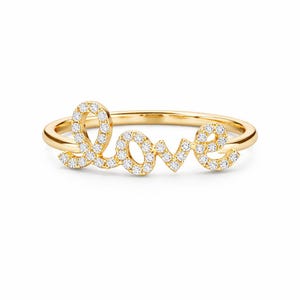 May include: A gold ring spelling out the word "love" in a cursive font. The letters are encrusted with small, sparkling diamonds. The band of the ring is a simple, polished gold.
