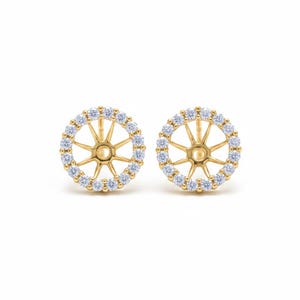 May include: A pair of gold-coloured stud earrings. Each earring has a circular design with a central starburst pattern and a halo of small, clear gemstones. The earrings are set against a white background.