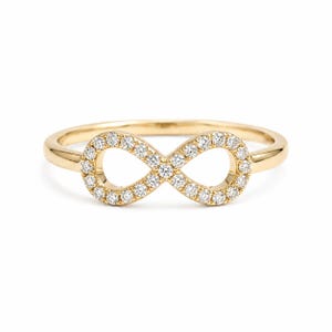 May include: A gold ring featuring an infinity symbol design. The infinity symbol is encrusted with small, sparkling diamonds. The ring has a polished, smooth band and a bright, reflective finish, perfect for everyday wear or special occasions.