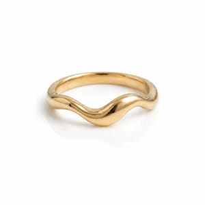 Può includere: Un anello in oro lucido caratterizzato da un design a fascia ondulata liscia e continua. Il metallo presenta una finitura riflettente e brillante che cattura la luce, creando una forma fluida e sinuosa che curva lungo la circonferenza.
