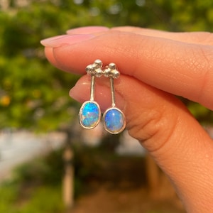 May include: A pair of silver earrings with a cluster of three small balls at the top and a blue opal stone at the bottom.