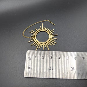 May include: Gold sunburst dangle earring with a chain and a small bead. The earring measures approximately 3 inches in diameter.