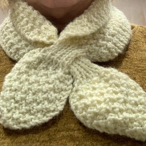 May include: A white knitted scarf with a unique knotted design. The scarf is made from soft, textured yarn and has a delicate, feminine look.