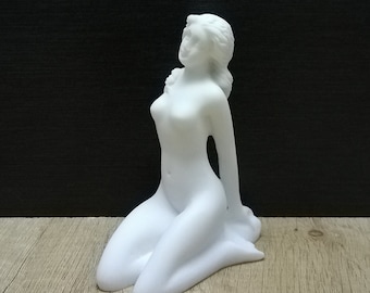 以下が含まれることがあります： 腕を組み、頭を後ろに傾けた座っている女性の白いセラミック彫刻です。