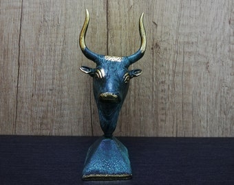 Puede incluir: Una escultura de toro verde azulado con cuernos dorados y una base cuadrada. La escultura está hecha de metal y tiene un diseño realista.