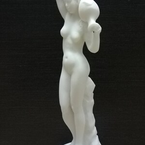 May include: White marble statue of a woman holding a pitcher above her head. The statue is standing on a square base.