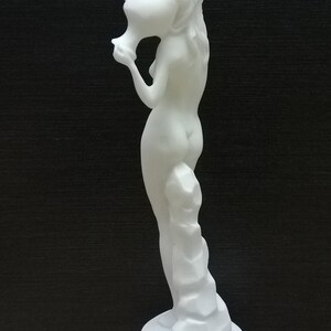 May include: White alabaster statue of a woman holding a pitcher. The statue is standing on a square base.
