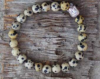 May include: A bracelet made of speckled brown and white beads with a silver clasp. The bracelet is lying on a piece of weathered wood.