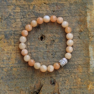 Puede incluir: Un brazalete de cuentas de color melocot&oacute;n con un dije de cabeza de Buda plateado. El brazalete est&aacute; hecho de cuentas redondas y est&aacute; enhebrado en un cord&oacute;n el&aacute;stico.