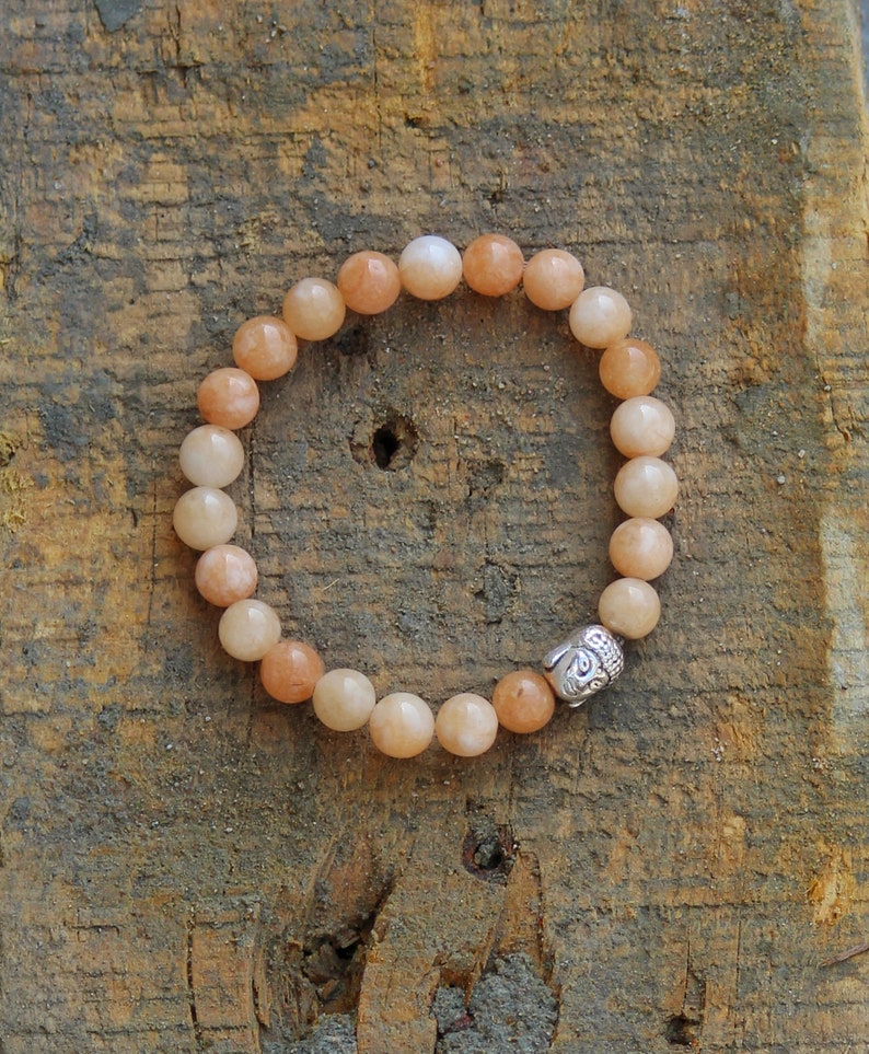 Puede incluir: Un brazalete de cuentas de color melocot&oacute;n con un dije de cabeza de Buda plateado. El brazalete est&aacute; hecho de cuentas redondas y est&aacute; enhebrado en un cord&oacute;n el&aacute;stico.