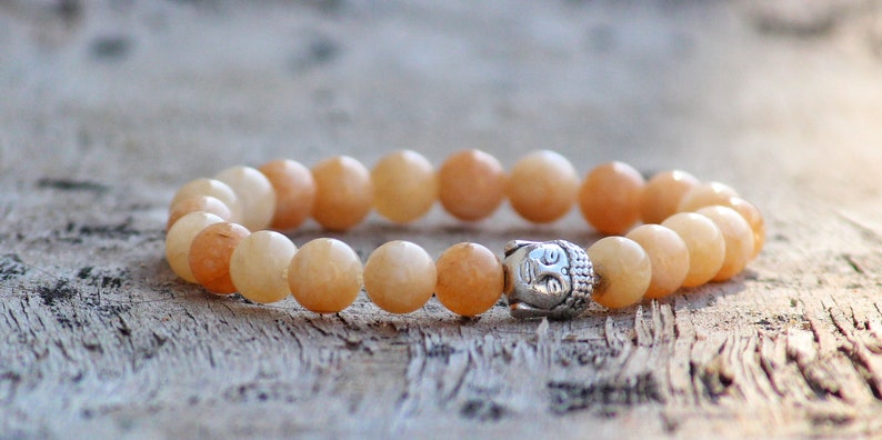 Puede incluir: Un brazalete de piedras preciosas de color naranja claro con un dije de Buda plateado. El brazalete est&aacute; hecho de cuentas redondas y est&aacute; enhebrado en un cord&oacute;n el&aacute;stico.