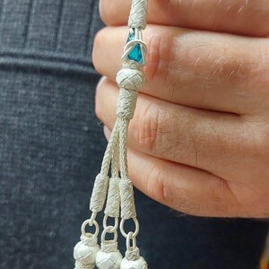May include: A white prayer beads with blue gemstone accents. The beads are strung on a white cord and have a tassel with three blue gemstones at the end.