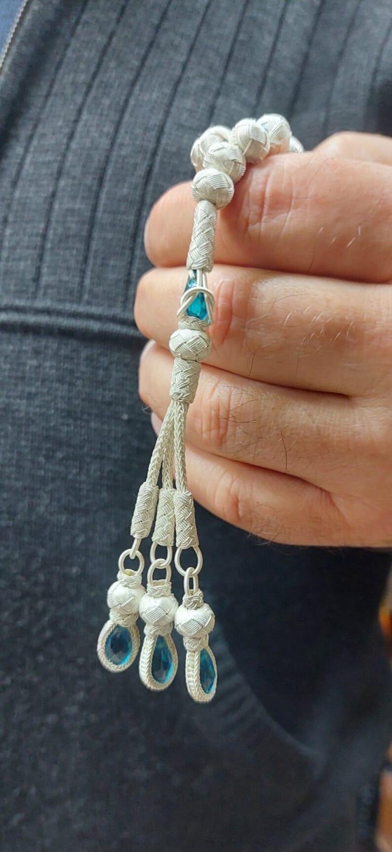 May include: A white prayer beads with blue gemstone accents. The beads are strung on a white cord and have a tassel with three blue gemstones at the end.