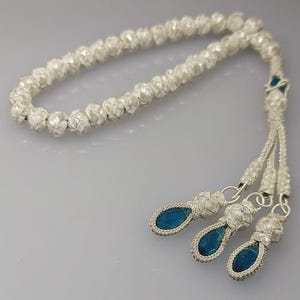 May include: A silver prayer beads necklace with three blue gemstone tassels.