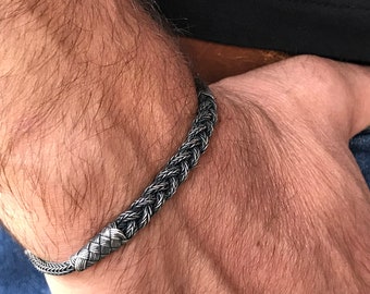 May include: A silver braided bracelet on a person's wrist.
