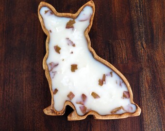 May include: A wooden dog-shaped tray with a white, glossy interior speckled with brown accents. The tray is set against a dark wood grain background, highlighting the natural wood tones of the tray's border.