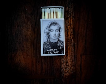 May include: A matchbox featuring a black and white image of Marilyn Monroe. The box includes the text "POLICE DEPT MINNEAPOLIS MINN 50177". The matches have light yellow tips.
