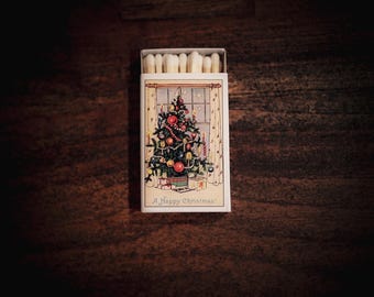 May include: A matchbox with a Christmas theme. The box features a festive illustration of a decorated Christmas tree with ornaments and gifts. The text "A Happy Christmas!" is printed at the bottom. The match heads are visible at the top.