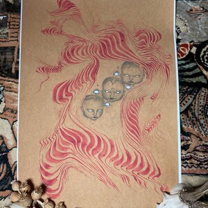 May include: A brown paper print with a red and white abstract design. The design features a series of wavy lines and four faces with large eyes.