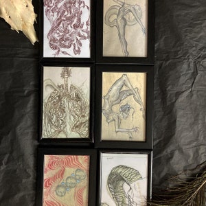 May include: Set of six framed art prints featuring black and white illustrations of figures and abstract designs. The frames are black with a white mat.