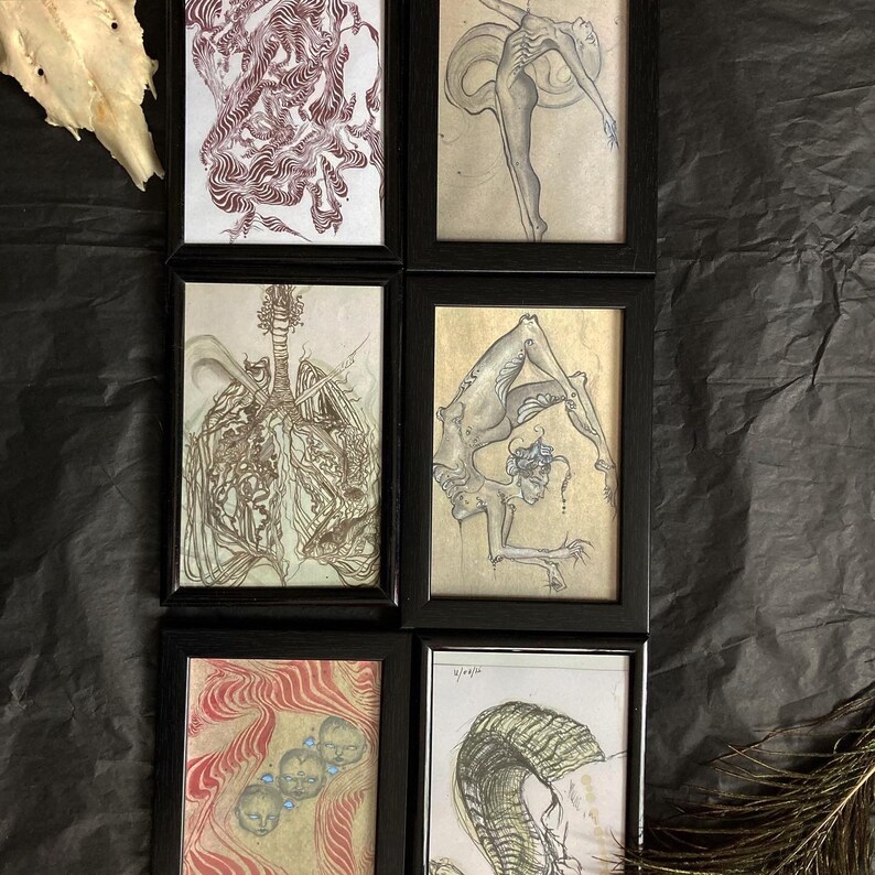May include: Set of six framed art prints featuring black and white illustrations of figures and abstract designs. The frames are black with a white mat.