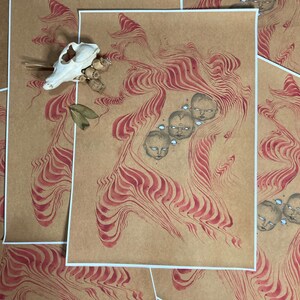 May include: A print on brown paper with a red and white swirling pattern. There are five small faces with closed eyes in the centre of the swirling pattern.