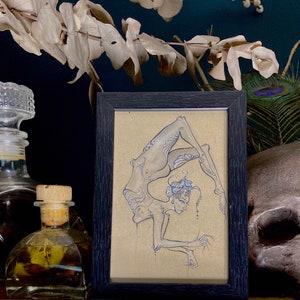 May include: A framed black and white drawing of a person in a contortionist pose. The drawing is on a beige background and is framed in a black frame.