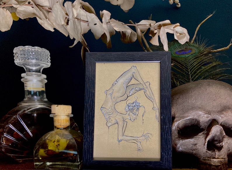 May include: A framed black and white drawing of a person in a contortionist pose. The drawing is on a beige background and is framed in a black frame.