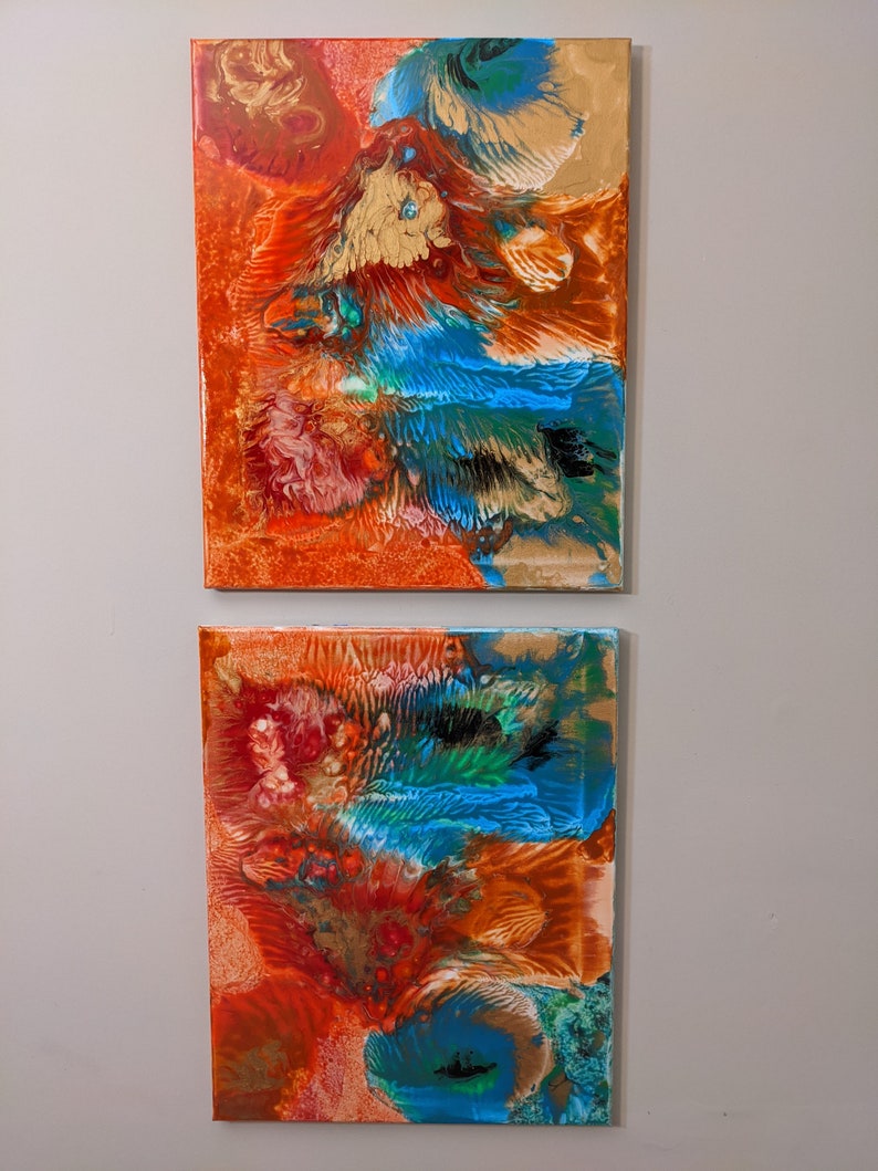 May include: Two abstract paintings on canvas with a mix of orange, red, blue, green, and gold paint. The paintings are displayed side-by-side on a wall.