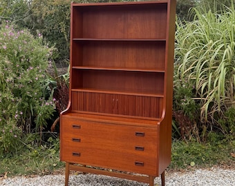 Op de afbeelding: Een hoge houten boekenkast met een warme bruine afwerking, voorzien van drie open planken aan de bovenzijde, een centraal kastgedeelte met twee kleine verticale deuren en drie horizontale lades aan de basis, rustend op vier taps toelopende poten.