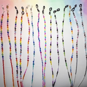 May include: A collection of twelve eyeglass chains made from faceted, multi-colored crystal beads. Each chain features small, clear or black rubber loops at the ends for attachment to glasses, with metallic connectors in gold or silver tones.