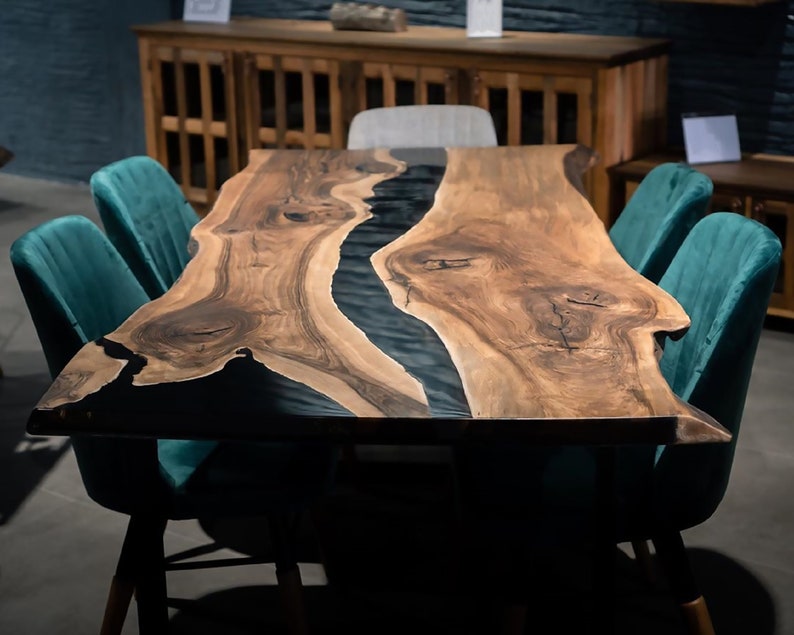 Puede incluir: Una mesa de comedor de borde vivo con un r&iacute;o de epoxi oscuro que atraviesa el centro. La mesa es de madera natural con un rico color marr&oacute;n y est&aacute; rodeada de sillas de terciopelo verde azulado. La mesa mide aproximadamente 183 cm de largo.