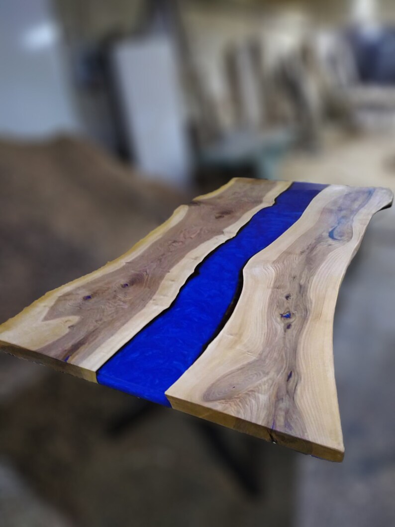Pu&ograve; includere: Un piano da tavolo in legno con un fiume di resina blu che attraversa il centro. Il legno ha una venatura naturale e la resina &egrave; liscia e lucida.