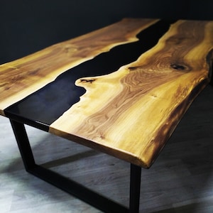 Puede incluir: Una mesa de madera hecha a mano con un r&iacute;o de resina epoxi negra en el centro. La mesa tiene un acabado de vetas de madera natural y se apoya sobre patas de metal negro. Las dimensiones de la mesa son de aproximadamente 183 cm de largo, 91 cm de ancho y 76 cm de alto.