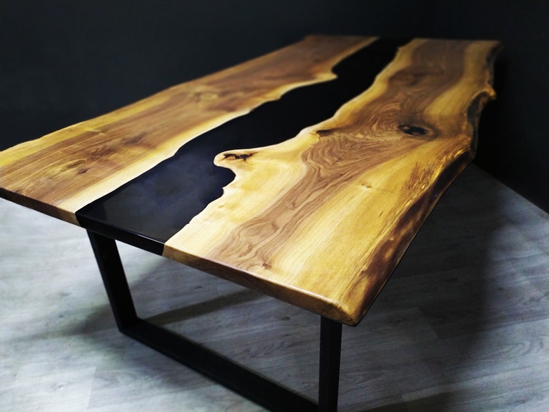 Puede incluir: Una mesa de madera hecha a mano con un r&iacute;o de resina epoxi negra en el centro. La mesa tiene un acabado de vetas de madera natural y se apoya sobre patas de metal negro. Las dimensiones de la mesa son de aproximadamente 183 cm de largo, 91 cm de ancho y 76 cm de alto.