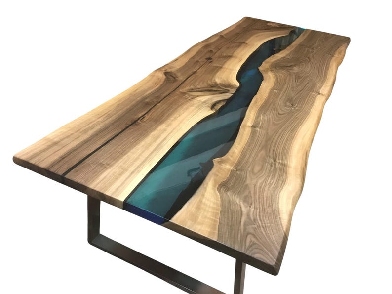 Puede incluir: Una mesa de comedor rectangular con un tablero de madera de borde natural y un patr&oacute;n de veta prominente. Un r&iacute;o de resina azul transl&uacute;cida recorre el centro de la madera. La mesa se apoya sobre una base de metal oscuro en forma de U.