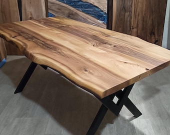 May include: A rectangular dining table featuring a natural live edge wood slab top with visible grain patterns and knots, supported by a black metal base with an X-shaped design. The wood surface displays light and dark brown tones.