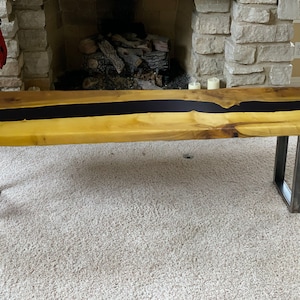 Può includere: Una panca in legno con un design a fiume in resina epossidica nera e gambe in metallo. La panca è su un tappeto beige chiaro.